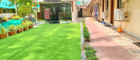 A hotel entrance with a green lawn, a tiled pathway, and a signboard.