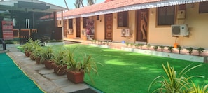 A building with a red-tiled roof, a green lawn, and several potted plants. - Ave maria Luxury Room and Apartment  (Colva)