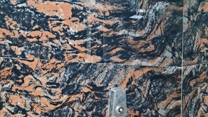 Un baño con pared de mármol, ducha con cabezal de ducha manual y bañera blanca.