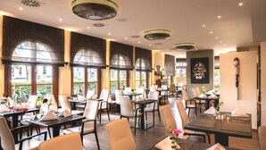 Un restaurante con varias mesas, sillas y vistas al exterior a través de amplios ventanales.