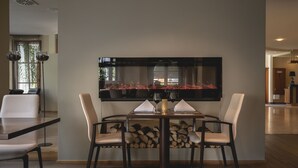 Un comedor con una mesa preparada para cuatro, sillas, una chimenea y un televisor de pantalla plana grande montado en la pared.