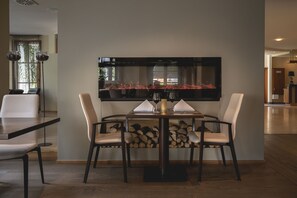 Un comedor con una mesa preparada para cuatro, sillas, una chimenea y un televisor de pantalla plana grande montado en la pared.