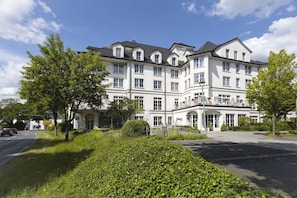 Een meerlaags hotel met een symmetrische gevel, grote ramen en een verzorgde tuin ervoor.
