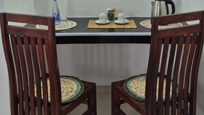 A dining area with a table set for two, two wooden chairs with patterned cushions, a water bottle, a box of tissues, and a kettle on the table. - NATIVE SOULS Beach Hotel (Induruwa)