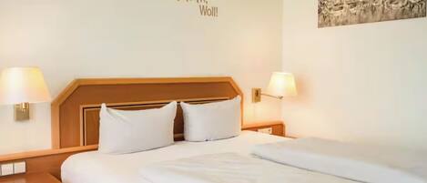 Habitación de hotel con una cama, dos lámparas de noche, un cabecero y una pared con un letrero.