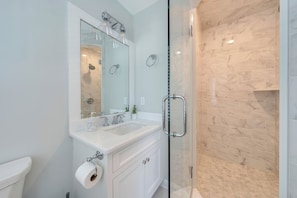 Une salle de bain avec une douche à parois de verre, un lavabo blanc et un miroir au-dessus.