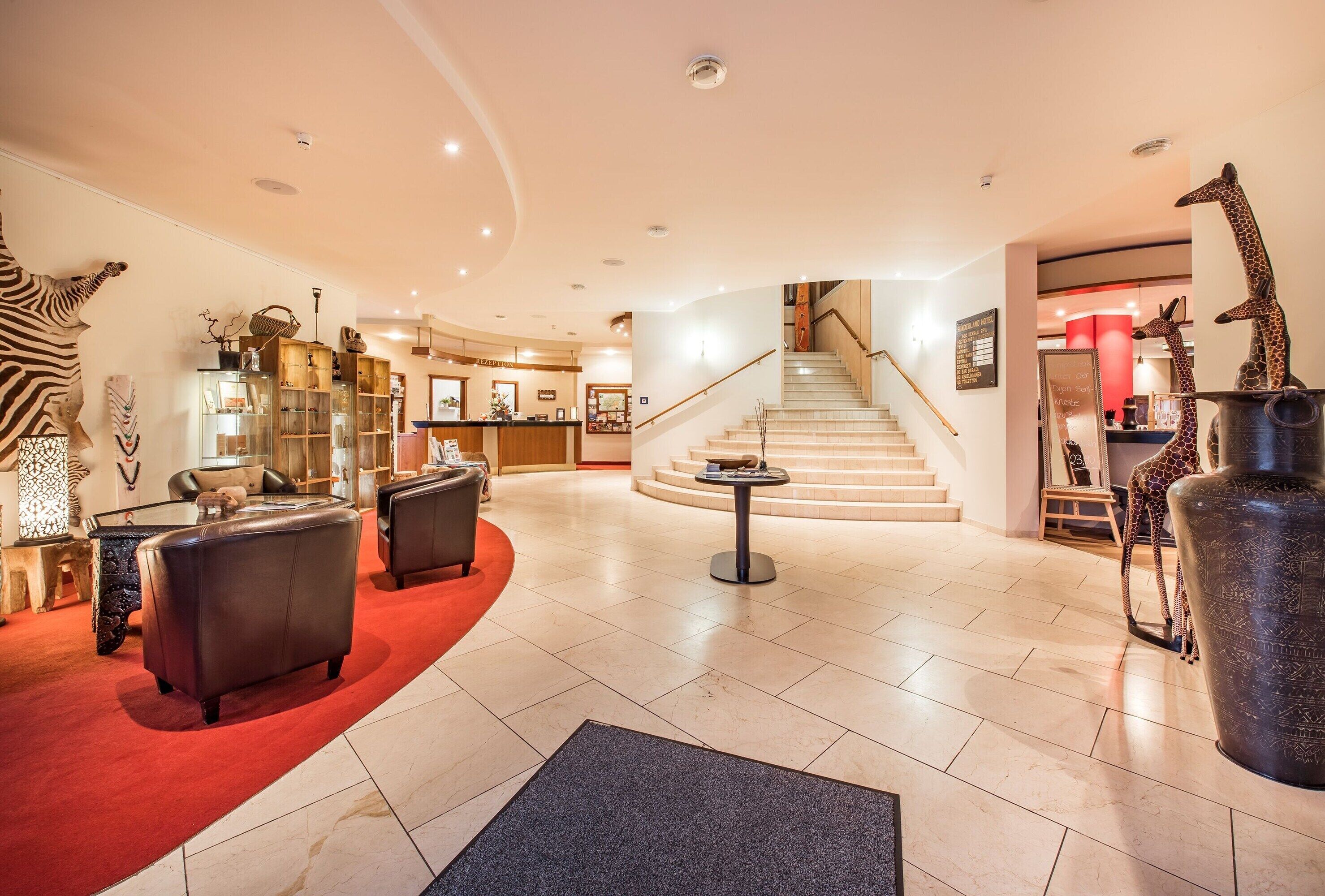 Eine Hotelhalle mit Empfangsschalter, Ledersofas, einer Treppe und dekorativen Giraffenskulpturen.