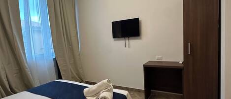 A hotel room with a bed, a desk, a TV, and a wardrobe.