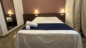 A hotel room with a bed, a nightstand, a mirror, and two wall-mounted lamps.