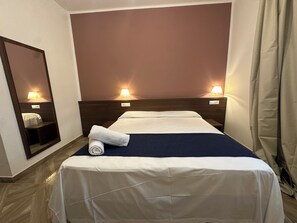 A hotel room with a bed, a nightstand, a mirror, and two wall-mounted lamps.