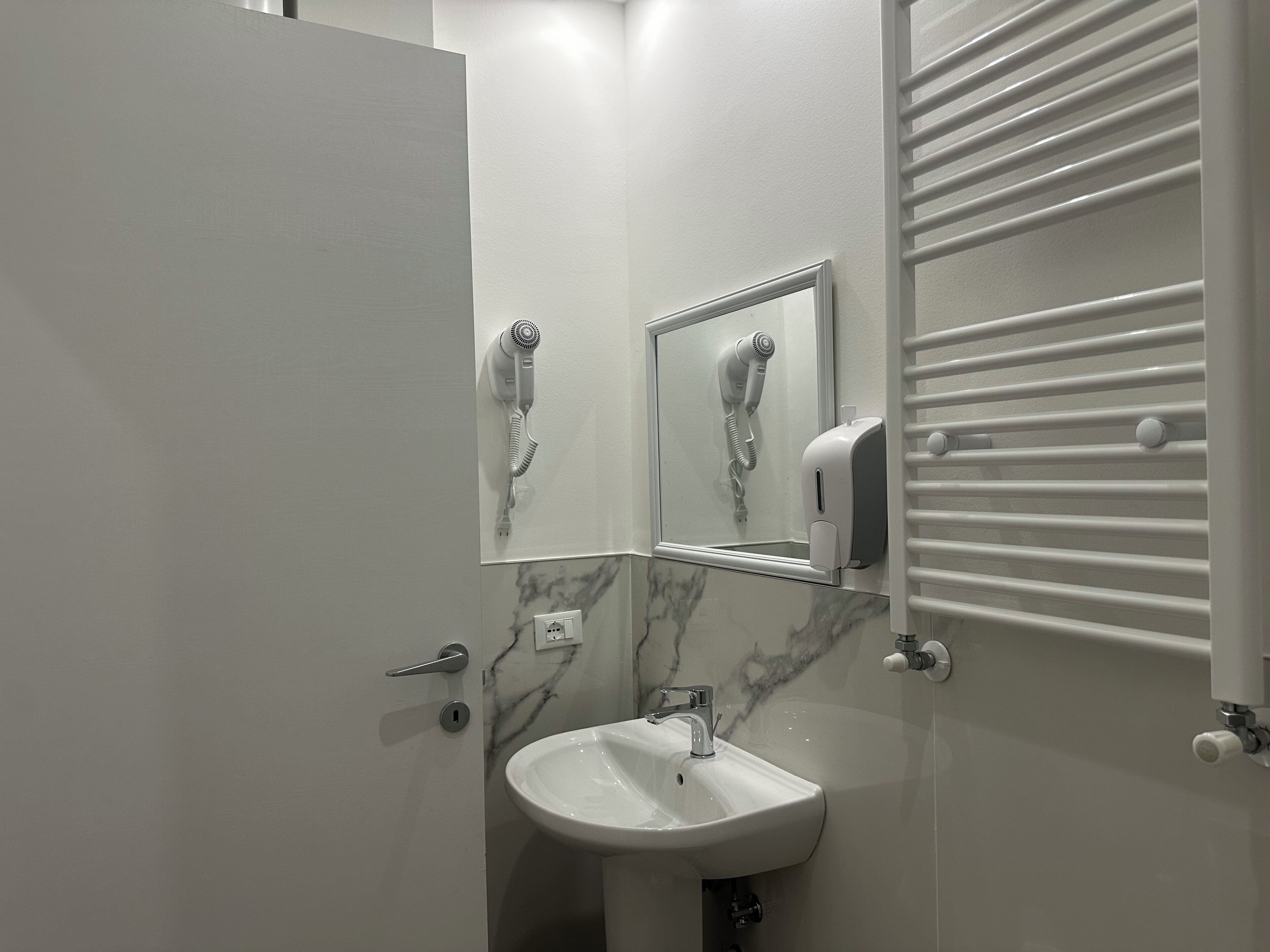 Ein Badezimmer mit einem weißen Waschbecken, einem Spiegel, einem Fön und einem Handtuchhalter.