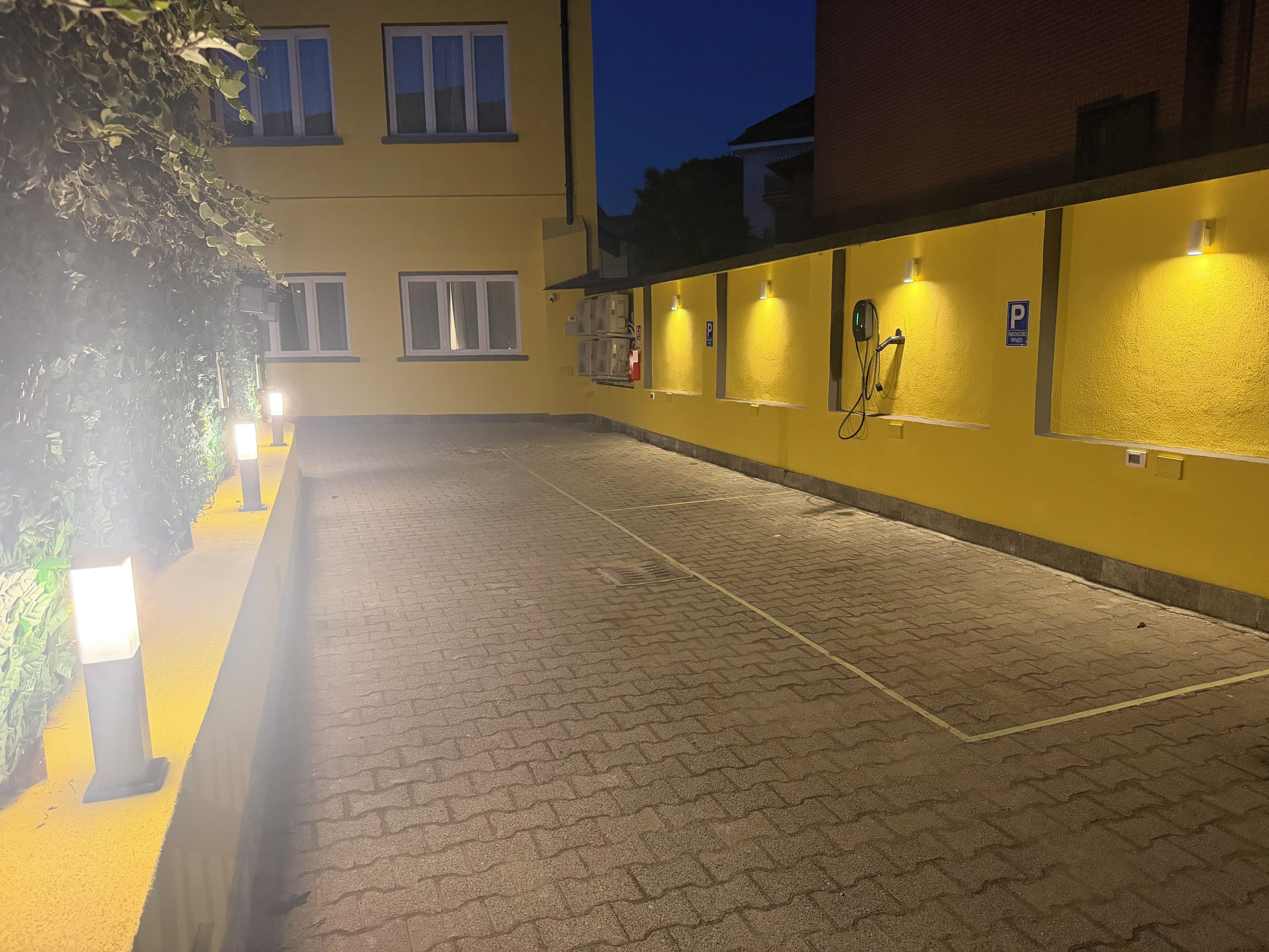 A paved outdoor area with a yellow building, a fire hose reel, and a parking sign.