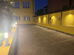 Un espacio al aire libre pavimentado con un edificio amarillo, un carrete de manguera contra incendios y un letrero de estacionamiento.