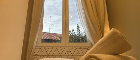 Una cama con una toalla enrollada, una ventana con cortinas y un diseño geométrico en la pared.