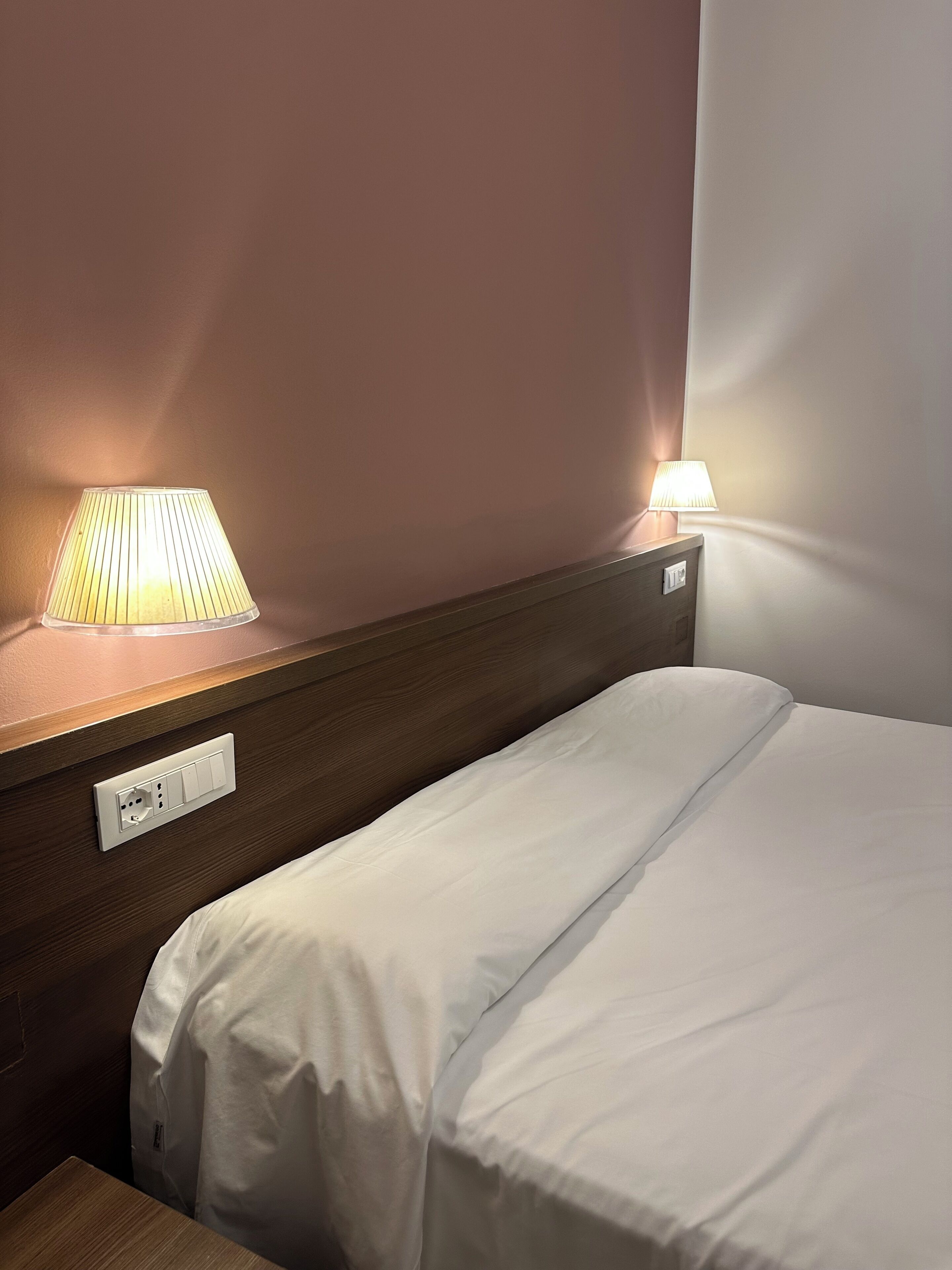 Una habitación de hotel con una cama, una mesita de noche y dos lámparas de noche.