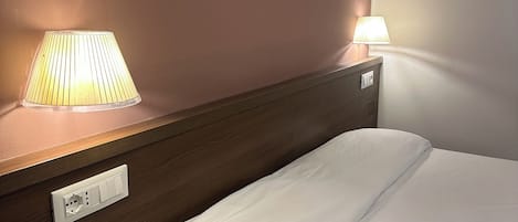 Una habitación de hotel con una cama, una mesita de noche y dos lámparas de noche.