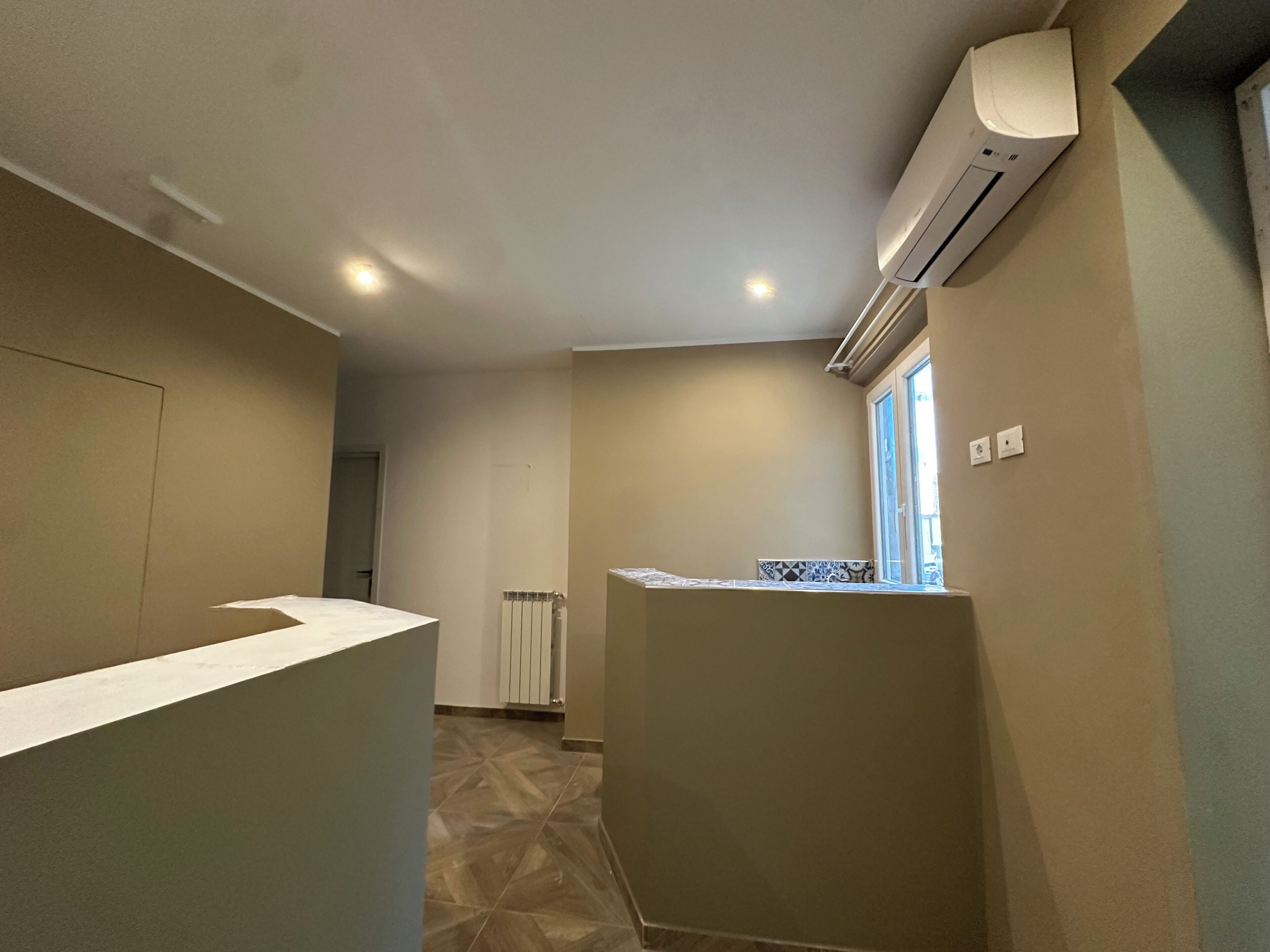 A hotel room with a kitchenette, a radiator, and a window with blinds.