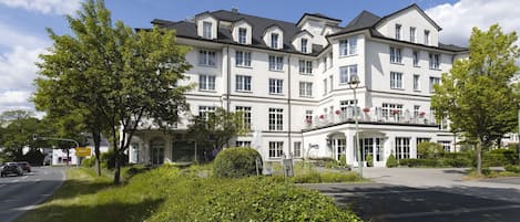 Un hotel de varios pisos con una fachada simétrica, amplias ventanas y un jardín bien cuidado al frente.