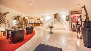 En hotellobby med reception, lædersofaer, en trappe og dekorative girafskulpturer.