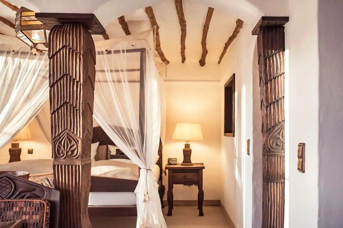 Una camera da letto con un letto a baldacchino, un comodino con una lampada e una porta in legno con un pannello decorativo.