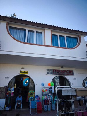 A two-story building with a pharmacy sign, outdoor seating area, and various items displayed outside. - Villa LINA, Beachfront (Fontane Bianche)