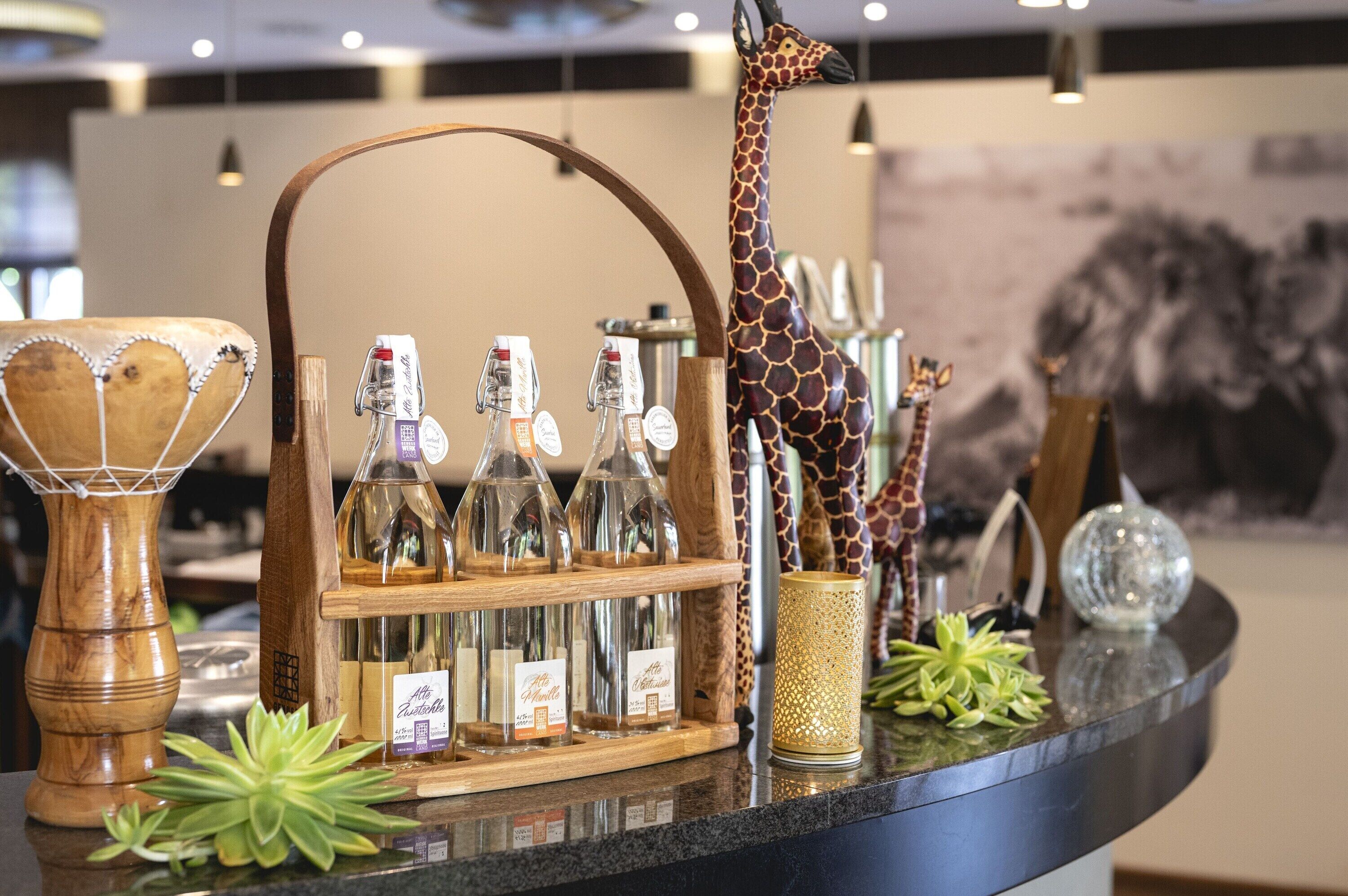 Eine Bar mit einer Holztrennwand, die mit Flaschen, einer Giraffenskulptur und Dekorationsgegenständen bestückt ist.