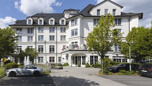 Un hotel a più piani con un ingresso imponente, una fontana e un'area di parcheggio con auto.