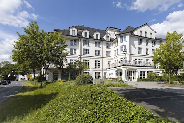 A multi-story hotel with a symmetrical facade, large windows, and a well-maintained garden in front.