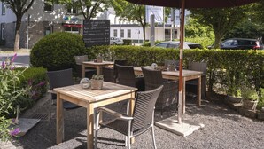 An outdoor seating area with tables and chairs, surrounded by greenery and a hedge. - Modern Escape Near Badehaus Norderney & Weststrand Beach l 2 Units (Sundern (Sauerland))