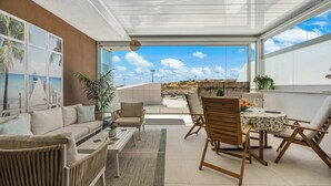 A modern living room with a sofa, chairs, a dining table, and a view of the sea through large windows. - Rooftop* Terrace*pool*parking* Town view (Estepona)
