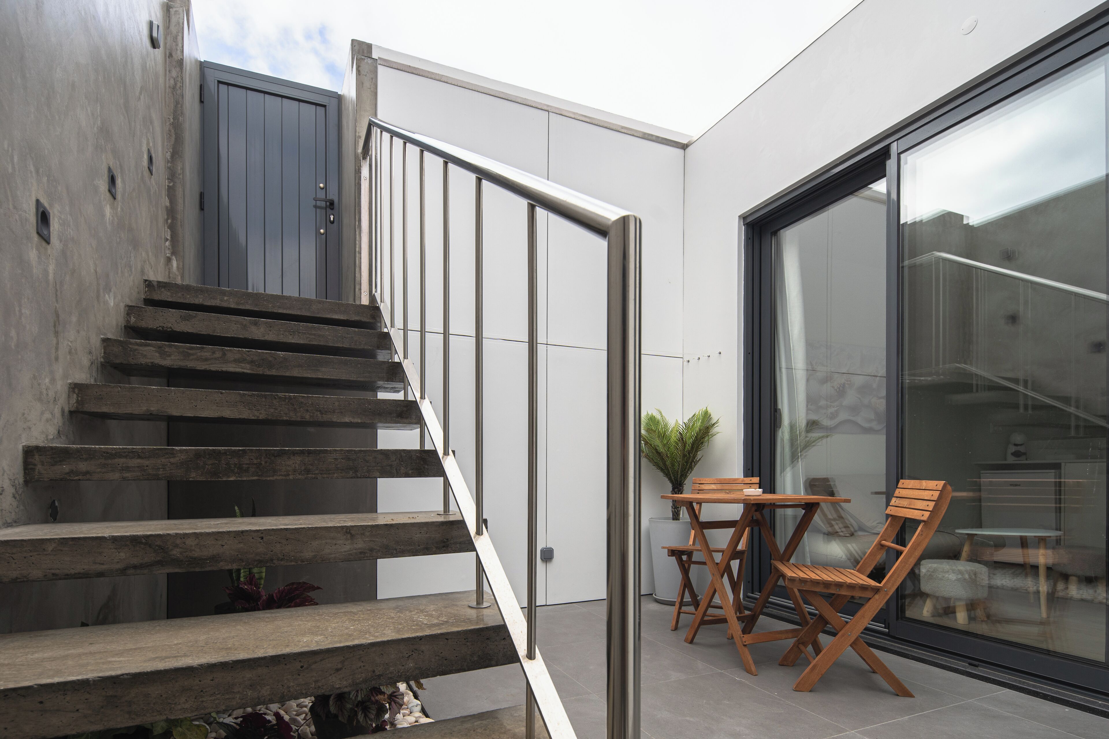 A modern outdoor staircase leading to a balcony with a table and chairs.