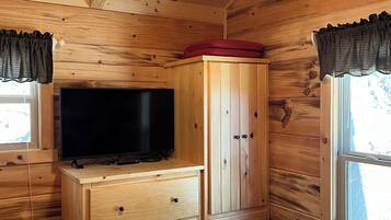 Ein Zimmer einer Holzhütte mit Deckenventilator, einem Fernseher auf einer Holzkommode, einem Kleiderschrank und einem Bett mit Steppdecke.