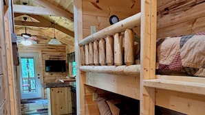 Ein Blockhaus-Innenraum mit Stockbett, Holzwänden, einer Küchenzeile und einem Esstisch.