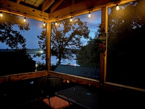A wooden deck with a table and chairs, overlooking a body of water and trees.
