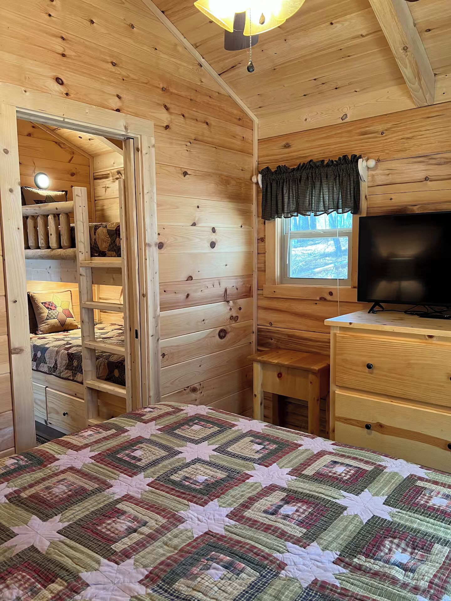 Una habitación de cabaña acogedora con una cama, un televisor y un ventanal con cortinas.