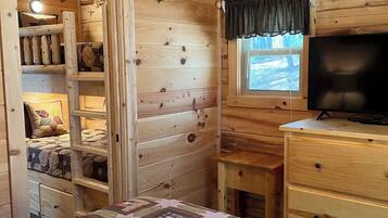 Una habitación de cabaña acogedora con una cama, un televisor y un ventanal con cortinas.