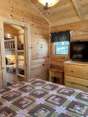 A cozy cabin room with a bed, a television, and a window with curtains.