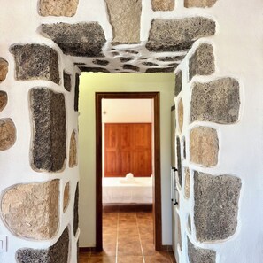 A hallway with stone walls and a wooden door leading to a room. - Casa Clarita (Tindaya)