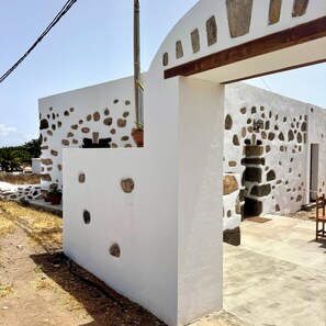 A building with a white exterior and stone accents, featuring a doorway and a small balcony with potted plants. - Casa Clarita (Tindaya)