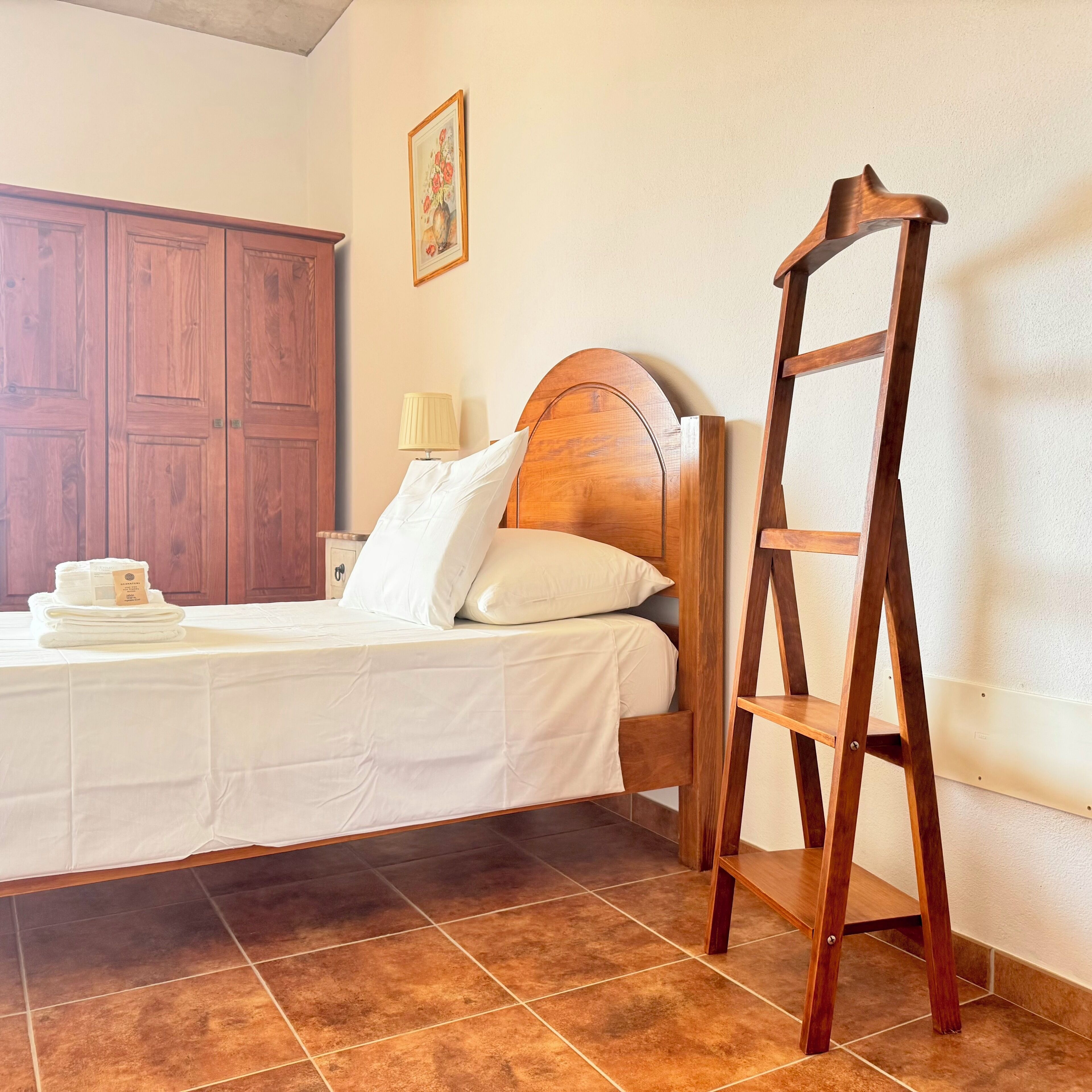 Un lit bien fait, avec une tête de lit en bois, une échelle en bois et une pile de serviettes sur une table.
