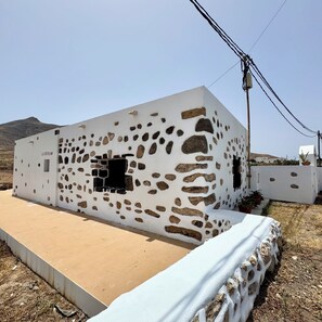A white building with stone patterns and a small window, set against a clear sky. - Casa Clarita (Tindaya)