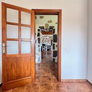 A wooden door with frosted glass panels leading to a hallway with stone walls and a tiled floor. - Casa Clarita (Tindaya)