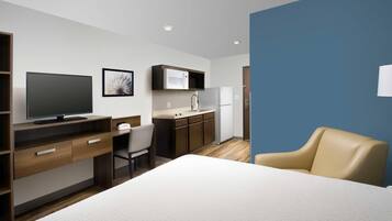 Ein Hotelzimmer mit einem Bett, einem Schreibtisch mit Computer, einem Sessel, einem Fernseher und einer Küchenzeile inklusive Mikrowelle und Spüle.