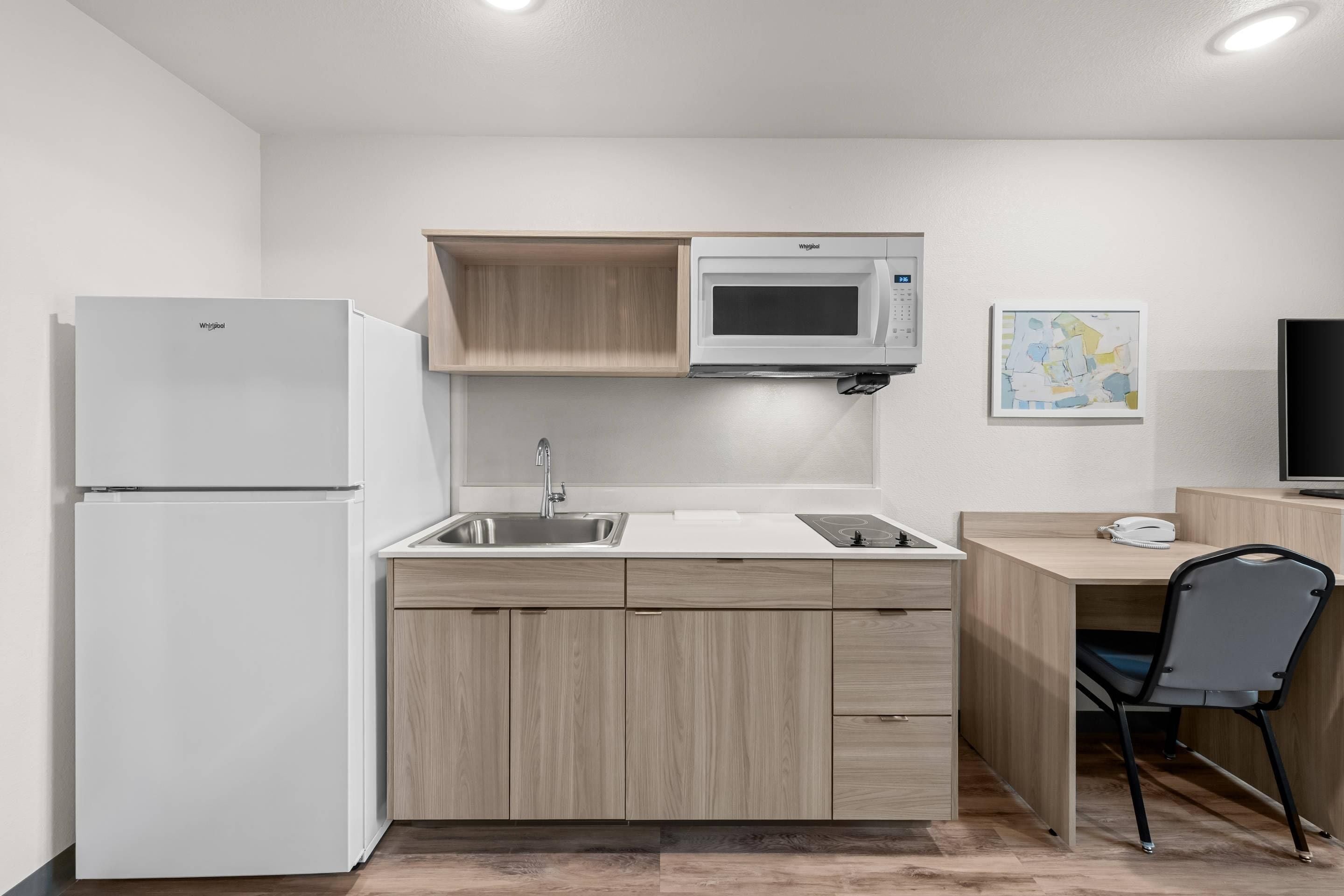 A compact kitchen with a refrigerator, microwave, sink, and a small desk area.