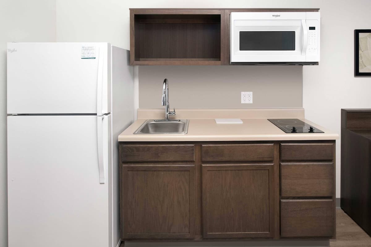 A compact kitchen with a refrigerator, microwave, sink, and wooden cabinets.