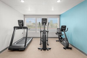 A gym with three cardio machines, a wall-mounted window, and a blue accent wall.