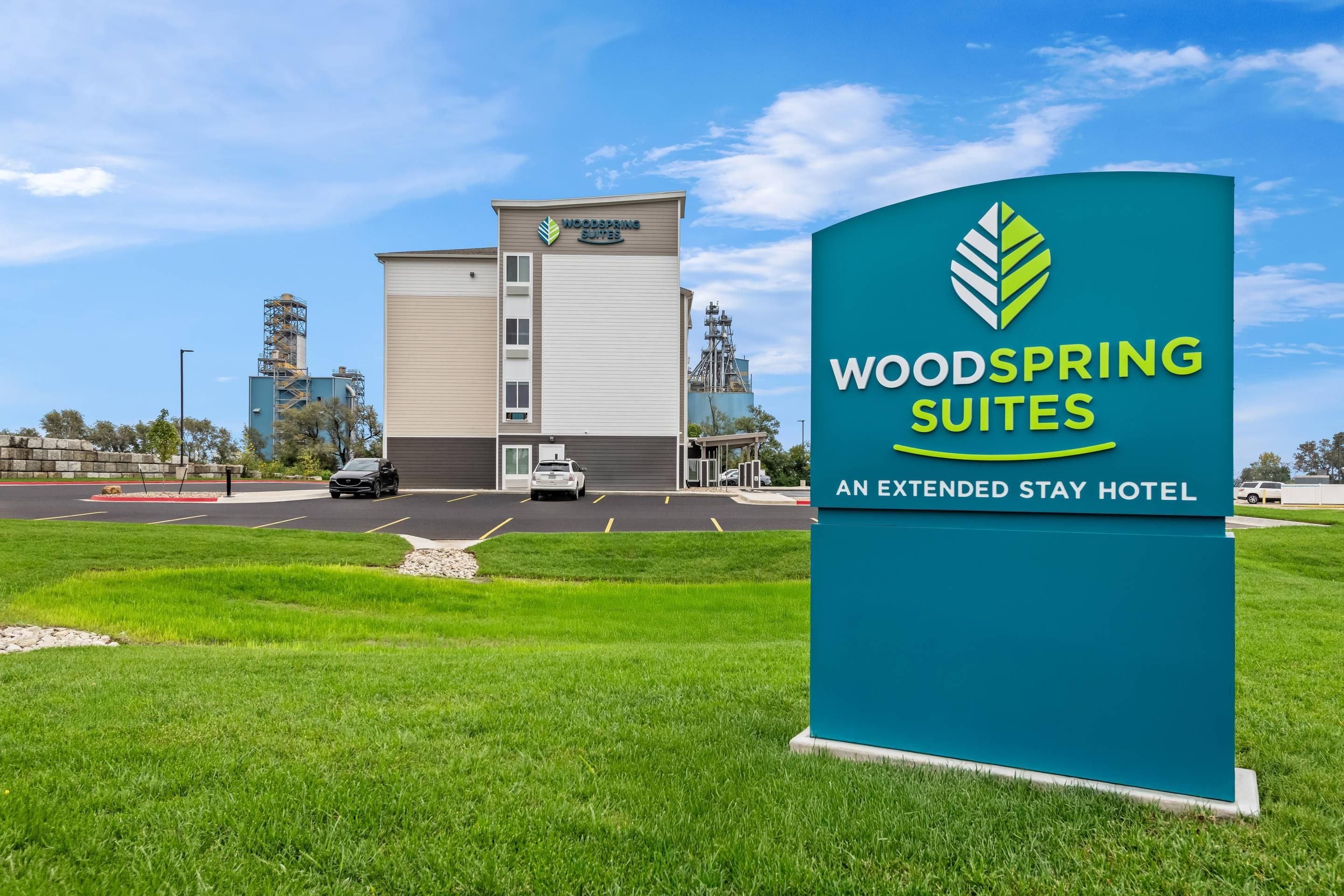 A hotel sign for WoodSpring Suites with a clear view of the building in the background.