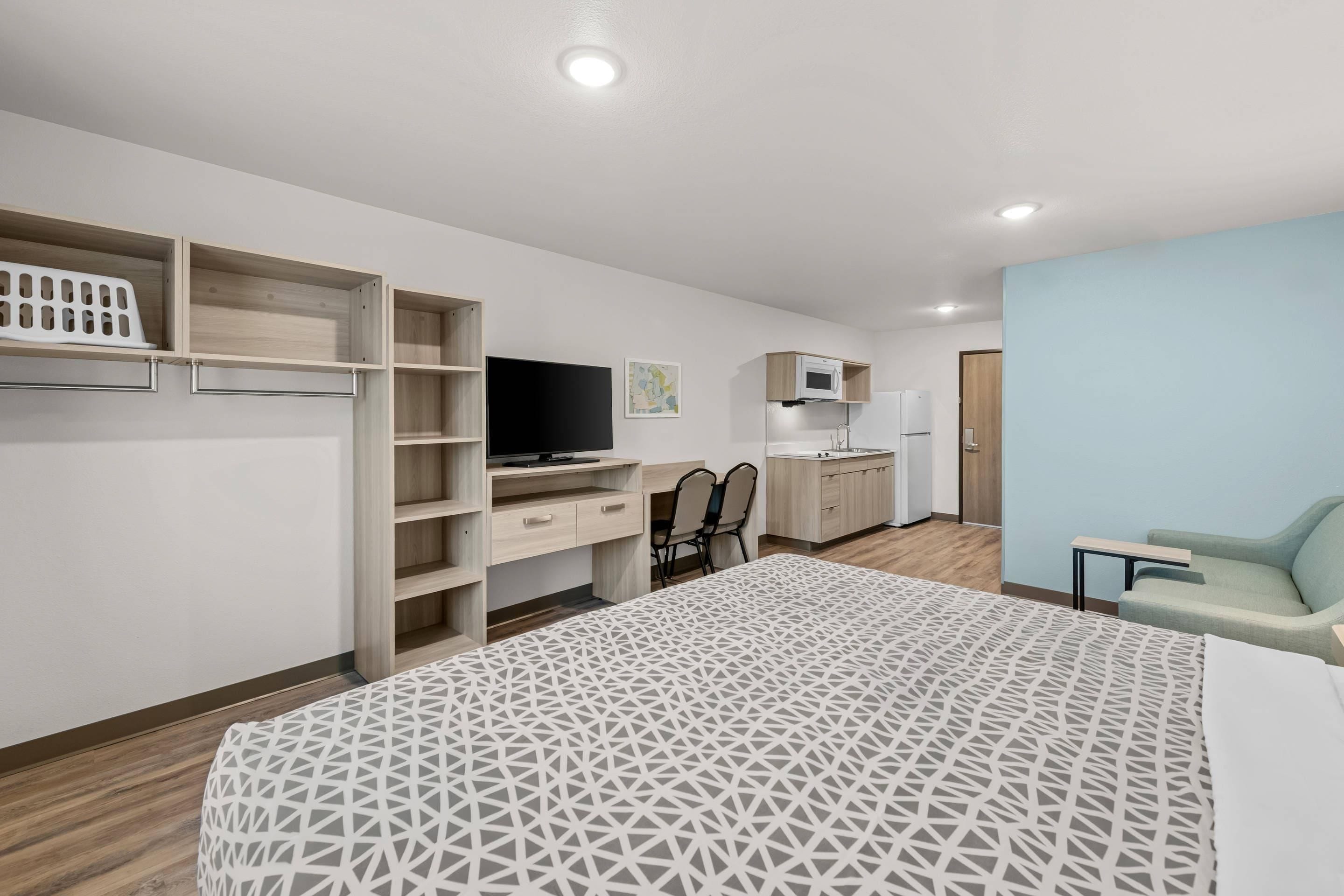 Ein modernes Schlafzimmer mit Bett, Schreibtisch, Fernseher und einer Küchenzeile.
