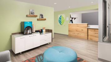 A modern hotel room with a kitchenette, a blue ottoman, and a patterned rug.