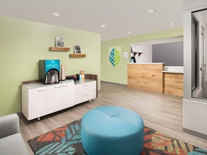 A modern hotel room with a kitchenette, a blue ottoman, and a patterned rug.
